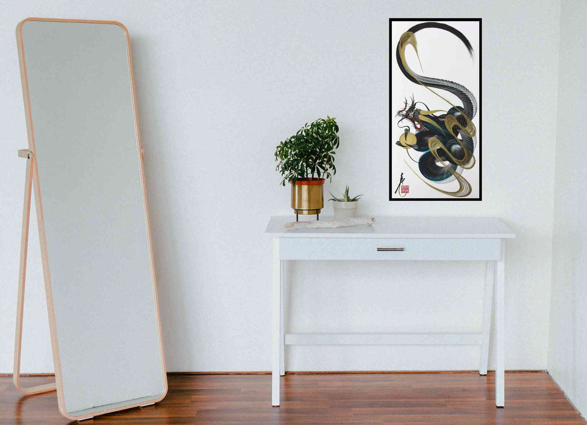 A framed vertical wall art print featuring an abstract black, gray, and gold snake-like design, displayed on a white console table in a minimalist room next to a tall floor mirror.